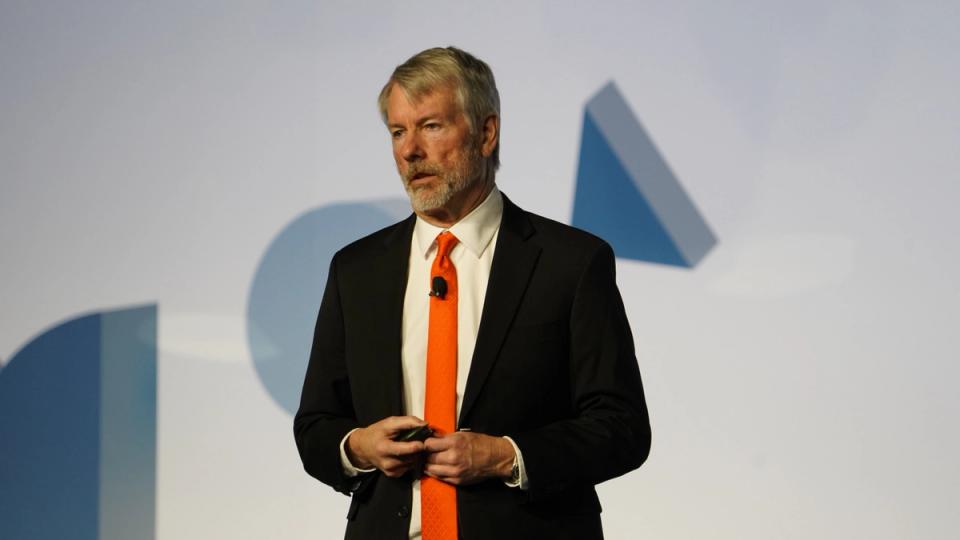 Michael Saylor at podium with Bitcoin logo and rising charts in background