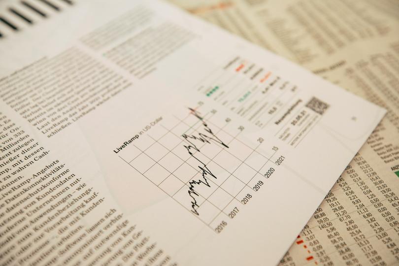 A digital graph showing a downward trend with a Bitcoin logo superimposed, with economic data charts in the background.