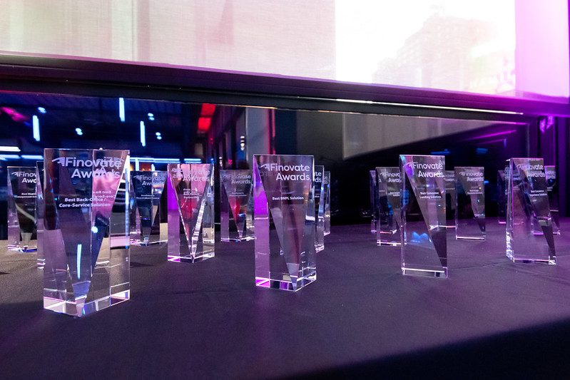 A fintech founder examining an innovation award trophy on their office desk, with laptop and pitch deck visible
